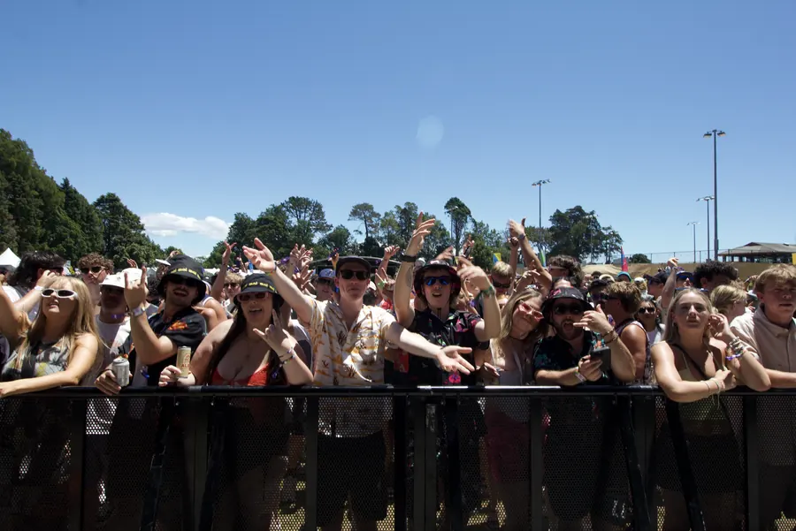 Crowd enjoying an outdoor concert on a sunny day at Bay Dreams 2024, some in sunglasses and hats, behind the front barrier.