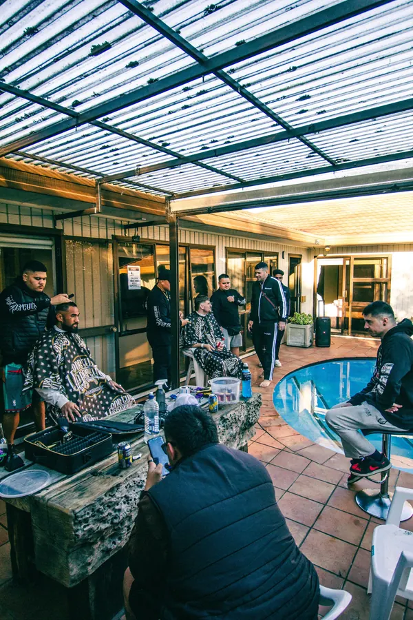 DJ set under a covered patio beside a pool at a house party, with guests gathered around the decks.