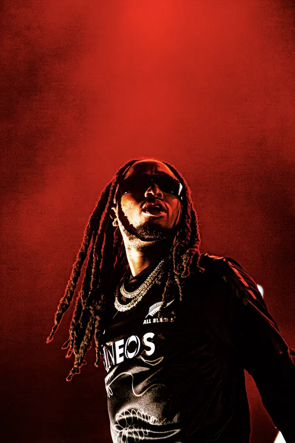 Quavo singing into a microphone against a red background.